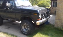 1979 Ford Bronco - A black Ford Bronco is parked outside a house, showing its front end and lifted suspension.