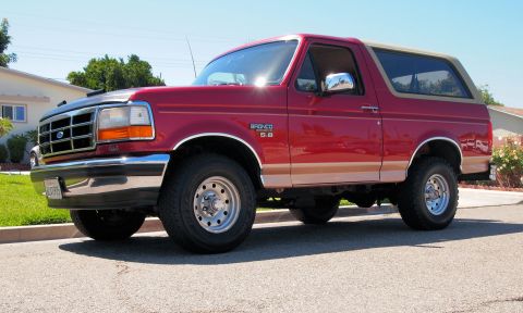 1994 Ford Bronco - This red 1994 Ford Bronco is parked on a residential street under a clear sky.