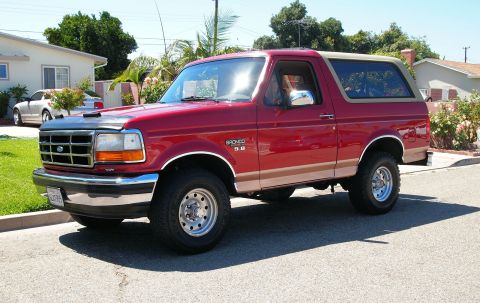 1994 Ford Bronco - A red 1994 Ford Bronco is parked curbside on a sunny day in a suburban neighborhood.