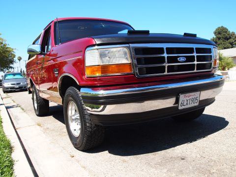 1994 Ford Bronco - Red 1994 Ford Bronco with chrome bumper and grille parked curbside under a clear blue sky.