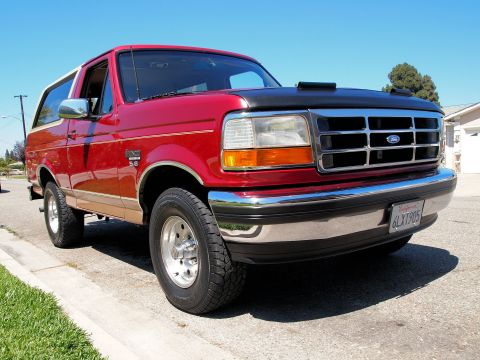 1994 Ford Bronco - This red Ford Bronco is parked curbside under a clear blue sky.