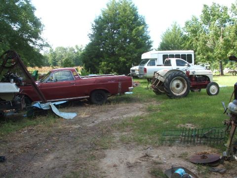1966 Ford Ranchero - A red 1966 Ford Ranchero sits in a yard next to a tractor and other vehicles.