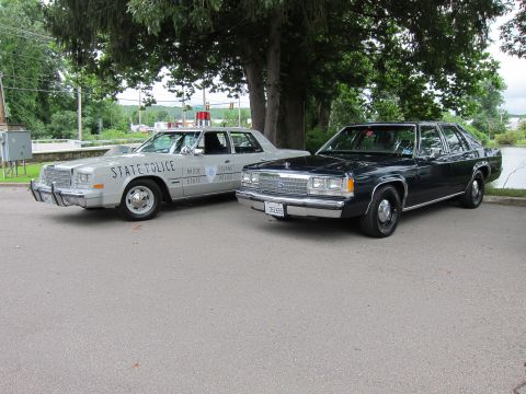 1991 Ford LTD Crown Victoria - silver Rhode Island State Police sedan parked next to a dark Ford LTD Crown Victoria on pavement near a waterway.