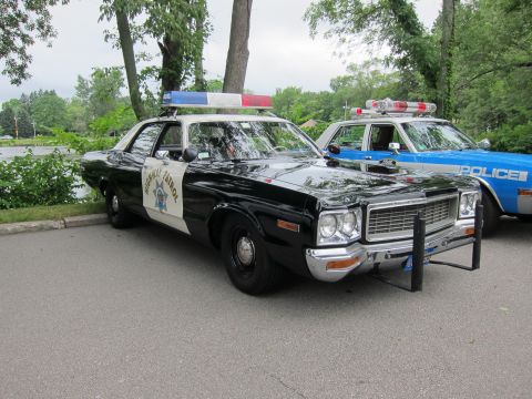 1991 Ford LTD Crown Victoria - black-and-white Highway Patrol sedan with push bumper parked beside a blue and white POLICE cruiser under trees.