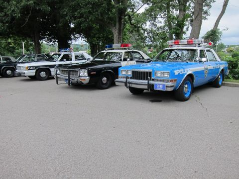 1991 Ford LTD Crown Victoria - row of vintage cruisers including a black-and-white car with push bumper and a blue POLICE sedan with plate 2440.