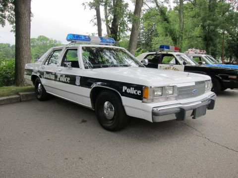 1991 Ford LTD Crown Victoria - black-and-white Boston Police Ford LTD Crown Victoria with roof lightbar parked under trees beside other cruisers.