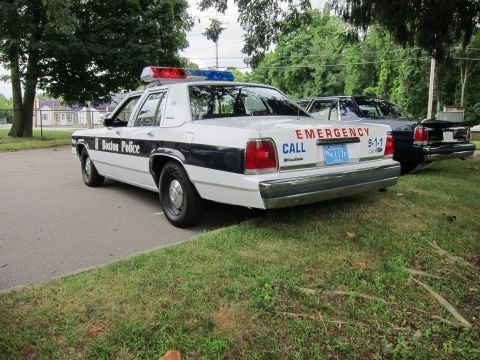 1991 Ford LTD Crown Victoria - Rear quarter view of a black-and-white Boston Police Ford sedan with red EMERGENCY CALL 9-1-1 lettering on the trunk.