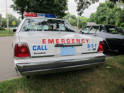 1991 Ford LTD Crown Victoria - Direct rear view of a white police Ford sedan with a lightbar and red EMERGENCY CALL 9-1-1 lettering across the trunk.