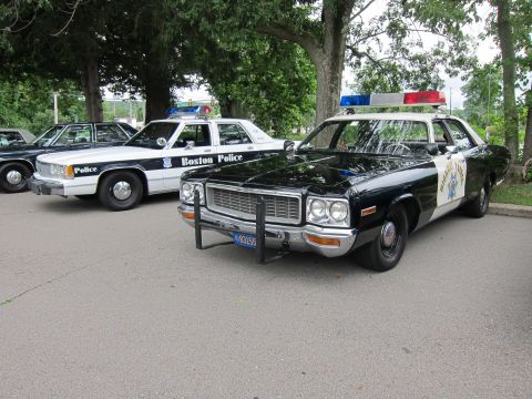 1991 Ford LTD Crown Victoria - black-and-white Highway Patrol sedan with push bumper parked beside a Boston Police Ford cruiser under trees.