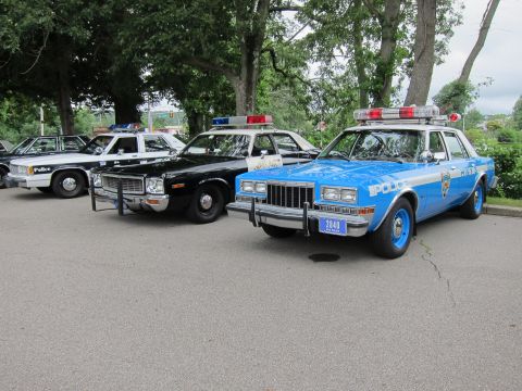 1991 Ford LTD Crown Victoria - Vintage cruisers parked in a row, including a black-and-white car with push bumper and a blue POLICE sedan with plate 2440.