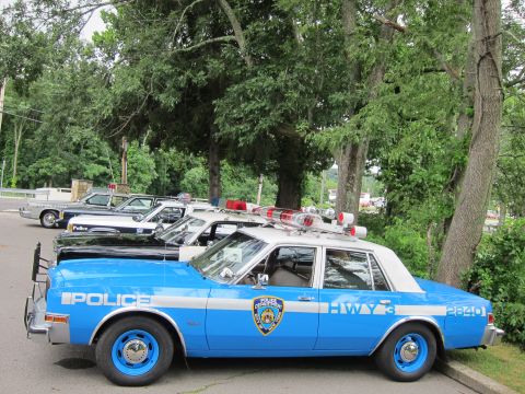 1991 Ford LTD Crown Victoria - Front three-quarter view of a blue NYPD 'POLICE HWY 3' patrol car with roof emergency lights, lined up with other restored police vehicles.