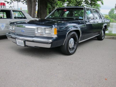 1991 Ford LTD Crown Victoria - dark blue Ford LTD Crown Victoria four-door sedan with chrome trim and dog-dish wheels parked beside a police cruiser near a lakeside lawn.