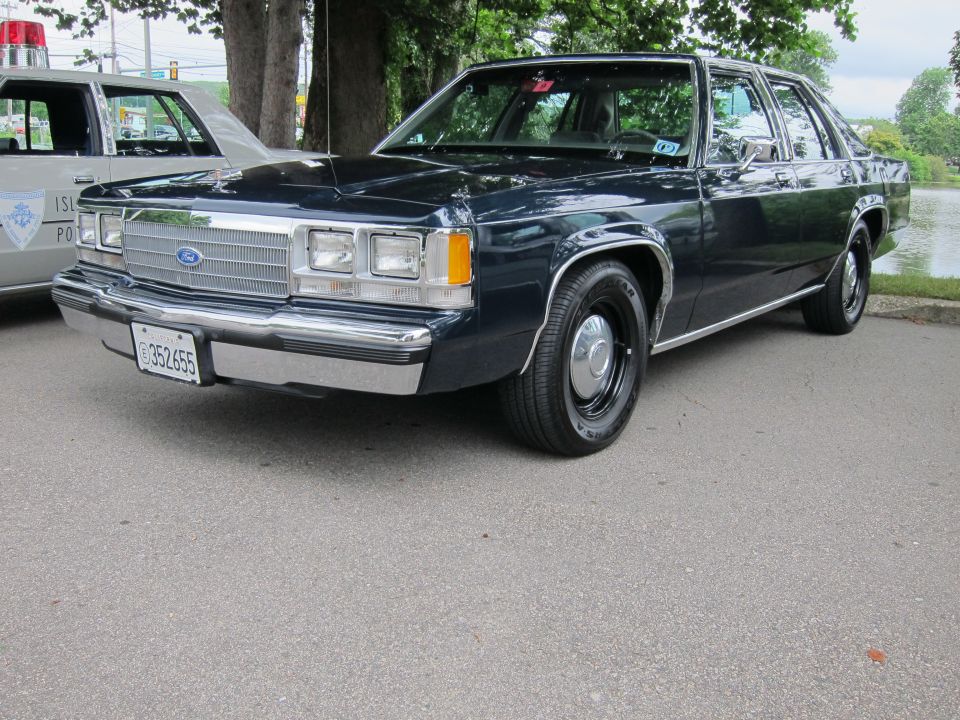 Dark blue Ford LTD Crown Victoria sedan parked near a lake beside a police car