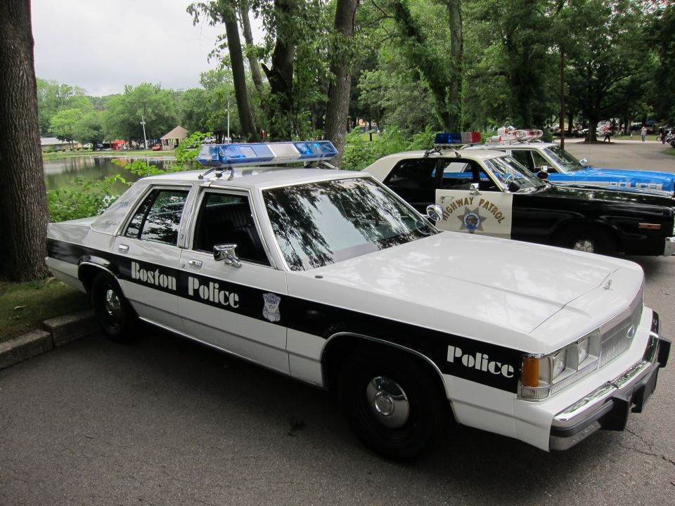 Black and white Boston Police Ford sedan parked by a pond with other cruisers