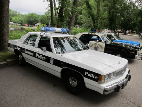 1991 Ford LTD Crown Victoria - Front three-quarter view of a black-and-white 'Boston Police' Ford sedan with roof emergency lights parked beside other classic patrol cars…
