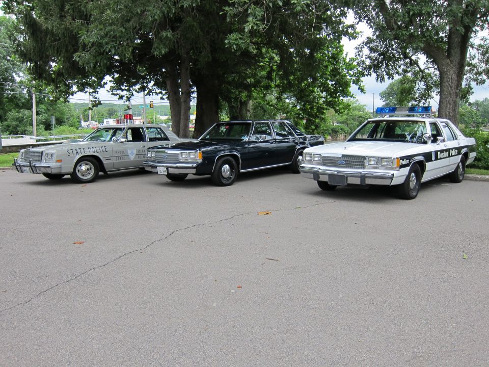 Three classic police cars including a State Police, dark sedan, and Boston Police lined up
