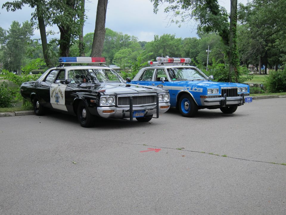 Two vintage police cars, a black highway patrol sedan and a blue NYPD cruiser, parked side by side