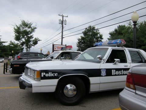 1991 Ford LTD Crown Victoria - Front three-quarter view of a black-and-white 'Boston Police' Ford cruiser with roof emergency lights in a lot near a Dunkin' Donuts sign.