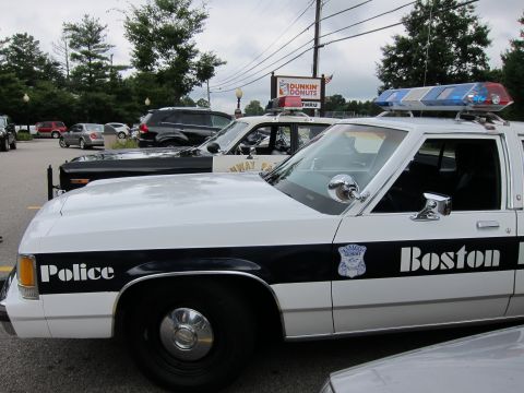 1991 Ford LTD Crown Victoria - Driver-side view of a black-and-white 'Boston Police' Ford cruiser with roof lightbar parked at a Dunkin' Donuts lot beside other police ca…