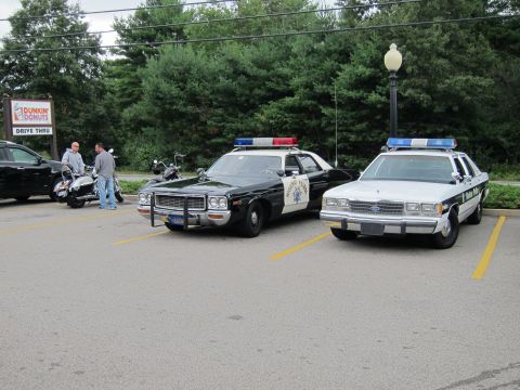 1991 Ford LTD Crown Victoria - black-and-white Highway Patrol sedan and a white-and-blue police cruiser parked in a Dunkin' Donuts lot with people and motorcycles nearby.