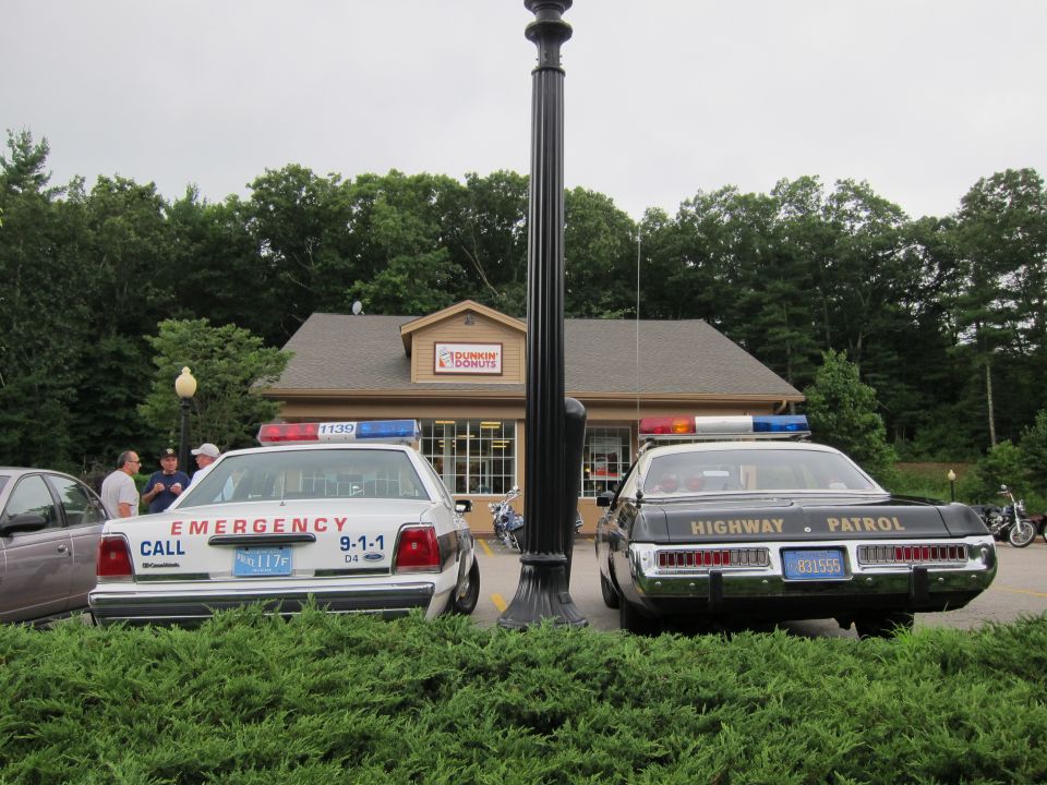 White EMERGENCY 911 Ford and black Highway Patrol car flank a lamppost at Dunkin Donuts