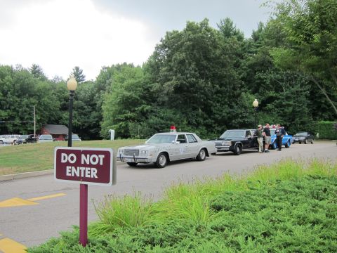 1991 Ford LTD Crown Victoria - maroon DO NOT ENTER sign stands before a row of parked classic American police sedans near woods.