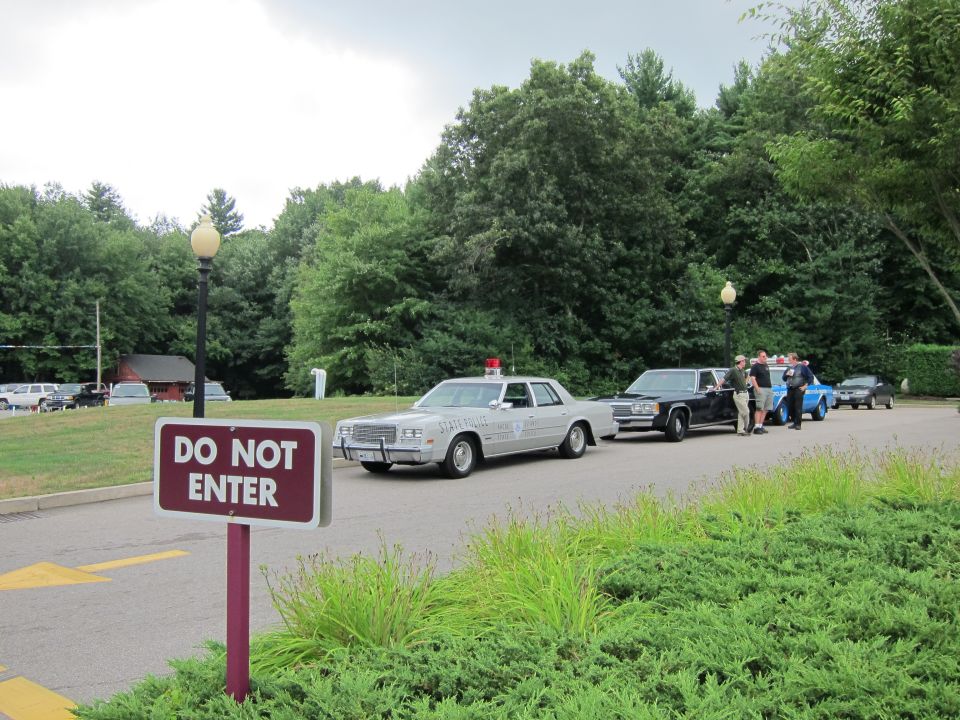 Maroon DO NOT ENTER sign with vintage police sedans parked beyond it