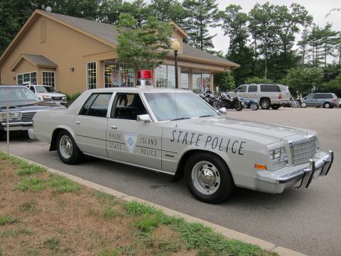 1991 Ford LTD Crown Victoria - silver four-door sedan lettered RHODE ISLAND STATE POLICE with a red roof light sits outside a tan building.