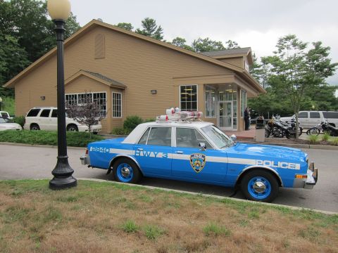 1991 Ford LTD Crown Victoria - blue-and-white NYPD Highway Patrol sedan marked HWY 3 with blue wheels parks beside a lamppost outside a tan building.