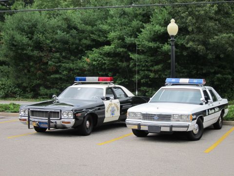 1991 Ford LTD Crown Victoria - black-and-white Highway Patrol sedan with a star door emblem parks next to a white-and-black police cruiser.