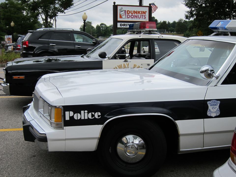 White-and-black Police cruiser front fender lettered Police by a Dunkin Donuts