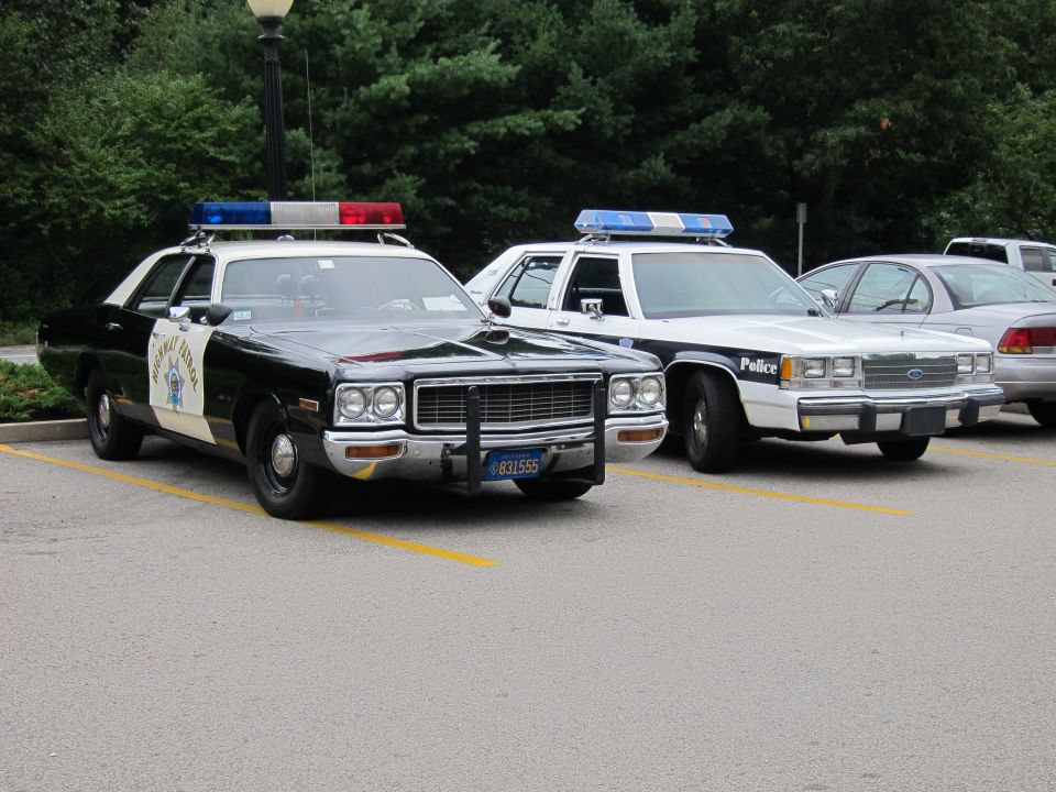 Black-and-white CHP-style sedan beside white police cruisers in a lot