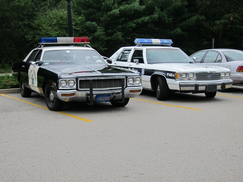 Black-and-white CHP-style sedan beside white police cruisers in parking lot