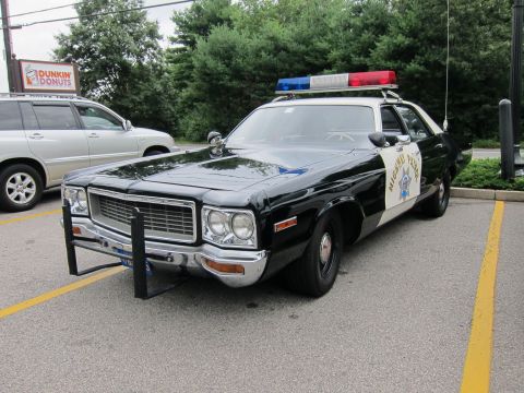 1991 Ford LTD Crown Victoria - Front three-quarter view of a black-and-white Highway Patrol sedan with chrome grille parked near a Dunkin' Donuts sign.