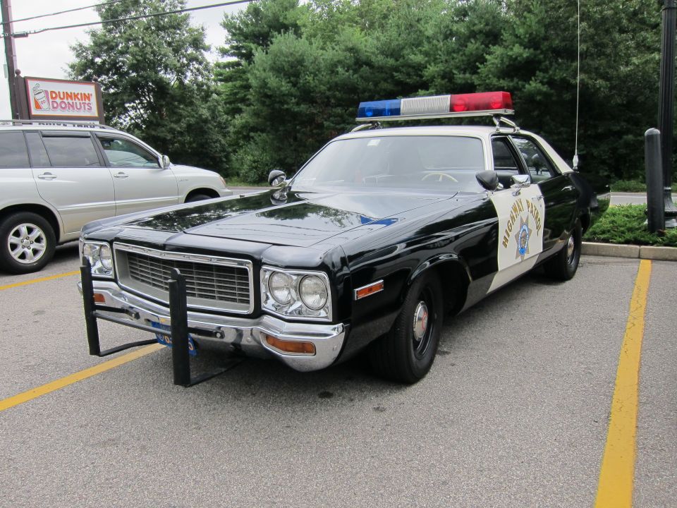 Black-and-white Highway Patrol sedan front view near a Dunkin Donuts sign