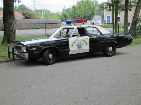 1991 Ford LTD Crown Victoria - black-and-white Highway Patrol sedan with white roof and door star emblem parks on a path beside a chain-link fence.