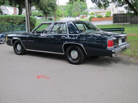 1991 Ford LTD Crown Victoria - Rear three-quarter view of a dark blue four-door sedan parked on a street, with a pink arrow painted on the pavement.