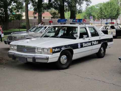 1991 Ford LTD Crown Victoria - white-and-blue Ford Boston Police sedan parks in front of a row of State Police cruisers on a paved lot.