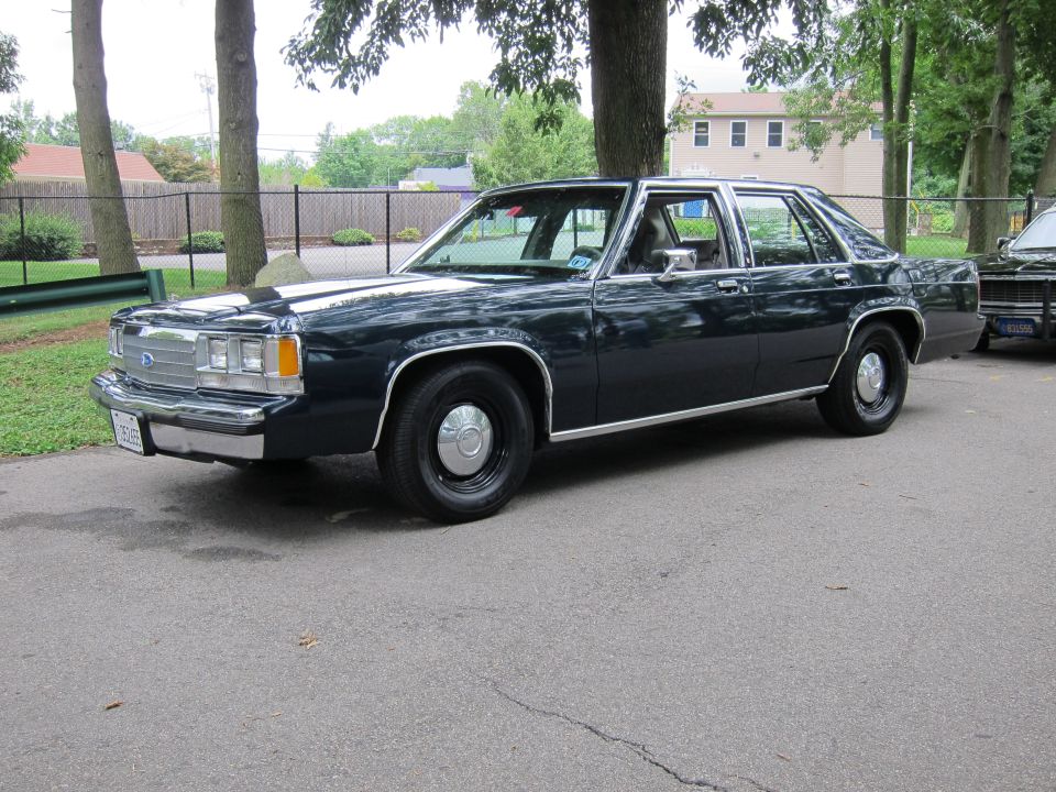 Dark blue four-door Ford sedan, front three-quarter view, parked on pavement