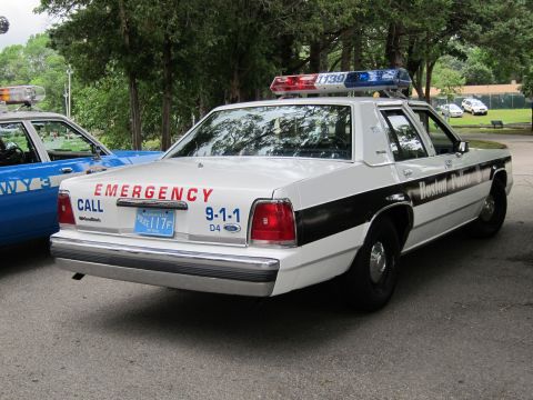 1991 Ford LTD Crown Victoria - Rear three-quarter view of a white Boston Police Ford sedan with EMERGENCY CALL 9-1-1 lettering and a roof lightbar.