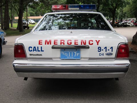 1991 Ford LTD Crown Victoria - Direct rear view of a white Ford police sedan lettered EMERGENCY CALL 9-1-1 with a Massachusetts POLICE 117F plate.
