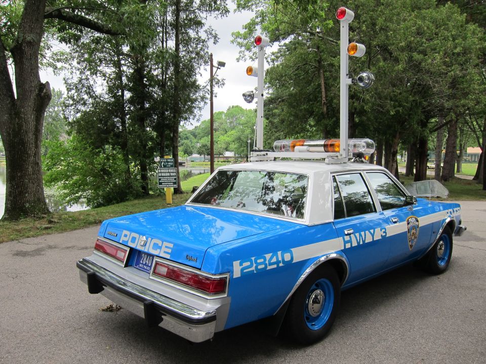 Blue NYPD Highway police sedan, rear three-quarter view with tall light poles