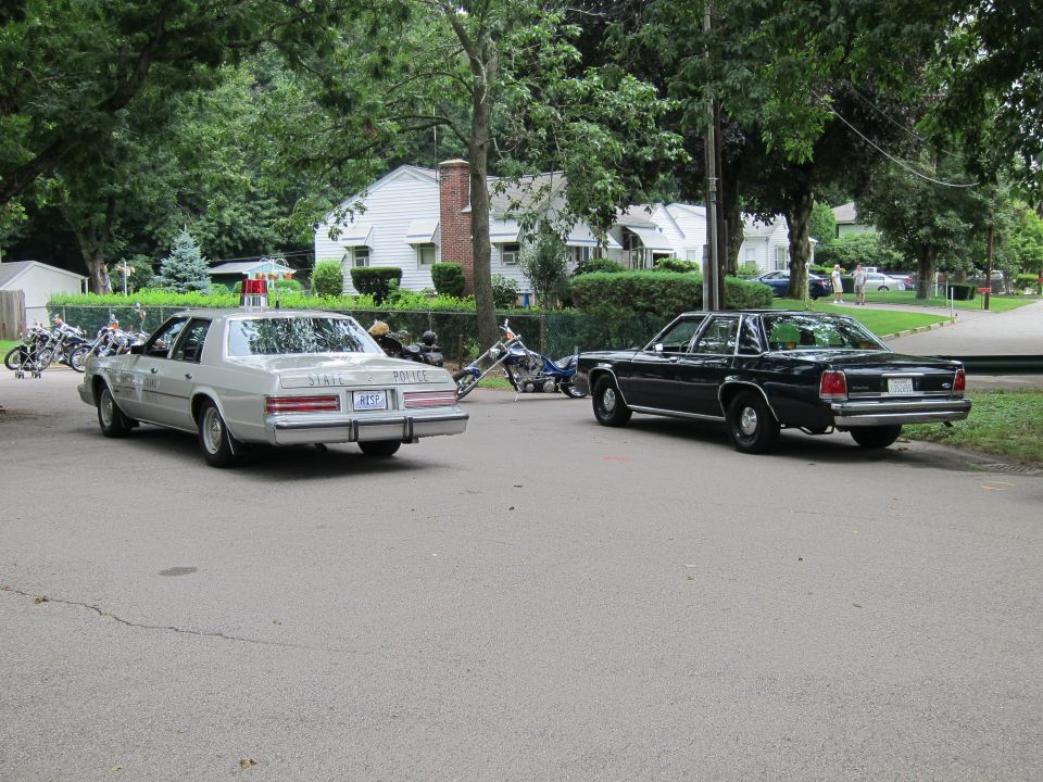 Silver State Police sedan and dark sedan parked across a lot, rear view