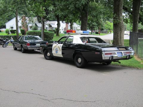 1991 Ford LTD Crown Victoria - black-and-white Highway Patrol sedan with white roof parked behind a dark sedan along a tree-lined residential lot.