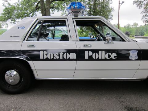 1991 Ford LTD Crown Victoria - Close driver-side view of a white-and-black Boston Police Ford sedan, unit 1139, with a blue roof beacon and door shield.