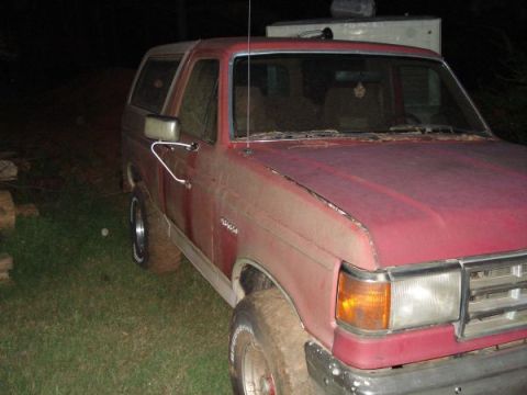 1995 Ford Bronco - A red Ford Bronco sits in a yard at night, showing its front and side profile.
