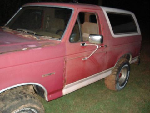 1995 Ford Bronco - A red and white Ford Bronco is shown from a 3/4 front angle, with visible wear and tear.