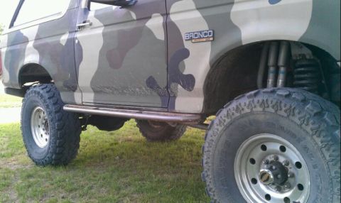 1995 Ford Bronco - This 1995 Ford Bronco features a camouflage paint job and aftermarket rock sliders, with a lifted suspension visible.