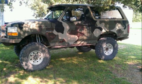 1995 Ford Bronco - This lifted Ford Bronco features a camouflage paint job and is parked outdoors on a grassy area.