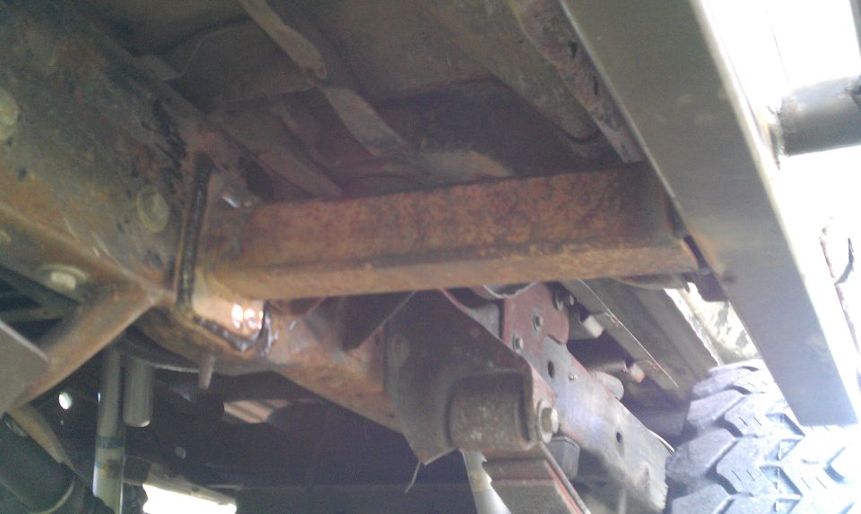 Undercarriage view of rusty frame and suspension components with a tire visible